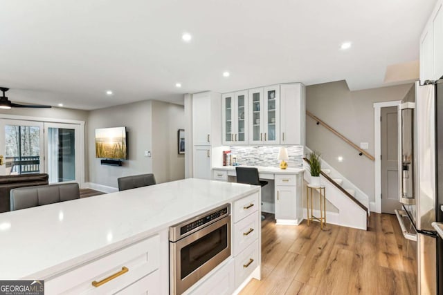 kitchen with stainless steel appliances, white cabinetry, light wood-style floors, light countertops, and decorative backsplash