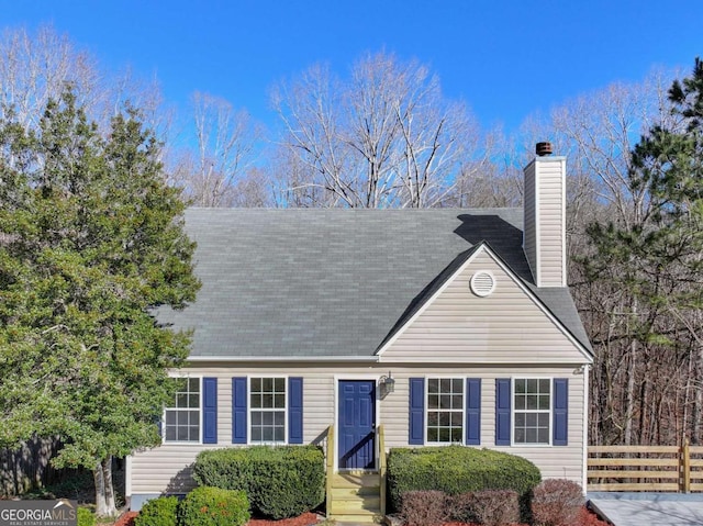 view of front of house featuring a shingled roof, a chimney, and fence