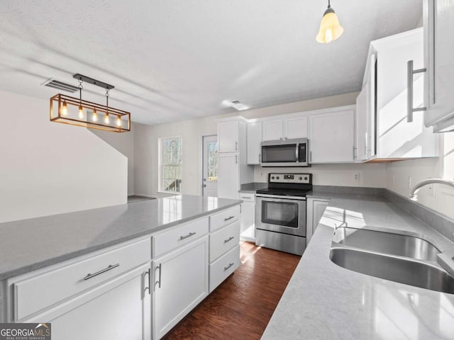 kitchen with dark wood-style flooring, decorative light fixtures, stainless steel appliances, white cabinets, and a sink