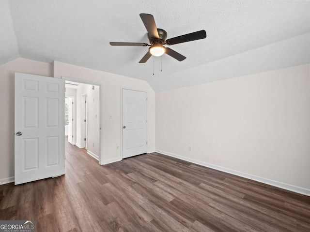 unfurnished bedroom with lofted ceiling, dark wood-style flooring, a textured ceiling, and baseboards