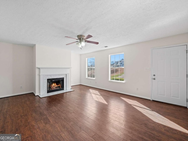 unfurnished living room with dark wood-style floors, a ceiling fan, a high end fireplace, and baseboards