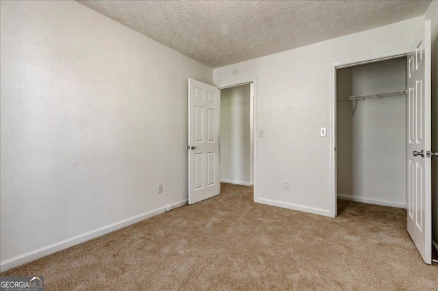 unfurnished bedroom featuring a closet, light colored carpet, a textured ceiling, and baseboards