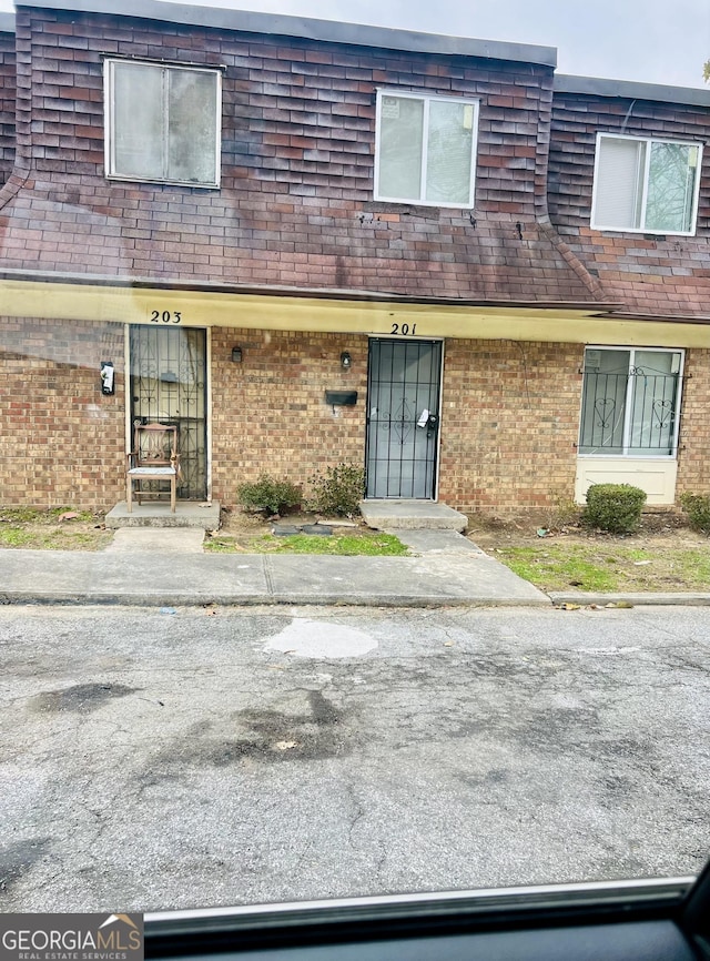 townhome / multi-family property featuring brick siding, roof with shingles, and mansard roof