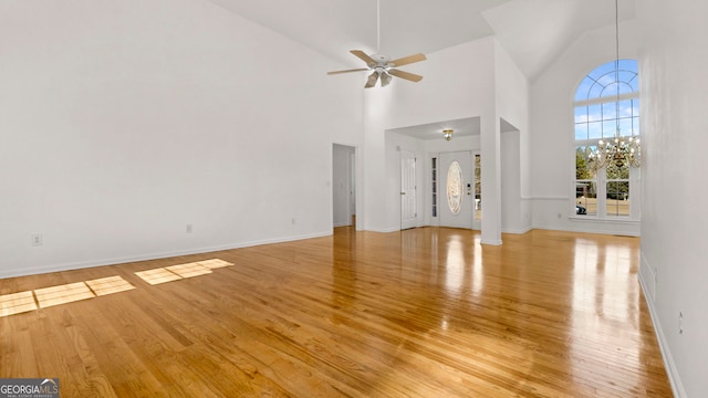 unfurnished living room with light wood-style floors, a high ceiling, baseboards, and a ceiling fan