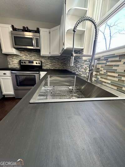 kitchen with stainless steel appliances, dark countertops, white cabinets, and a sink