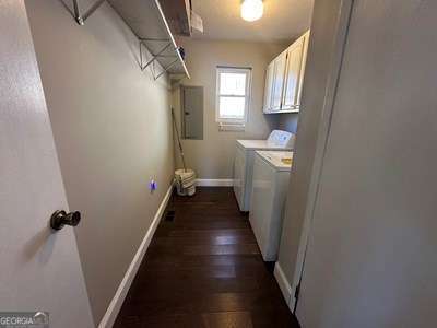 clothes washing area with washing machine and dryer, baseboards, cabinet space, electric panel, and dark wood-style floors