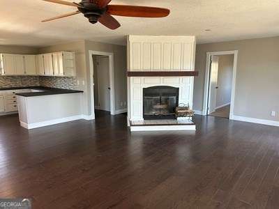 unfurnished living room featuring a large fireplace, ceiling fan, dark wood-type flooring, and baseboards