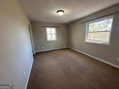 spare room with a textured ceiling, dark carpet, and baseboards