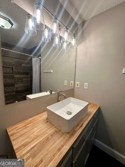 full bath with curtained shower, baseboards, vanity, and a textured ceiling