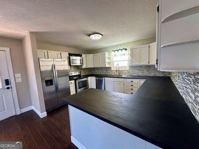 kitchen featuring tasteful backsplash, white cabinets, appliances with stainless steel finishes, dark wood-type flooring, and open shelves