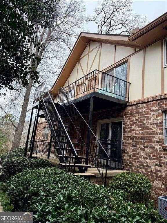 back of property featuring brick siding, stucco siding, a balcony, cooling unit, and stairs