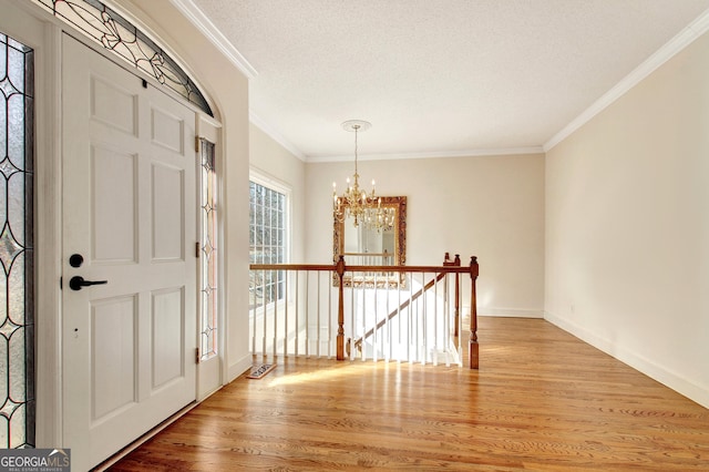 foyer featuring baseboards, light wood-style flooring, ornamental molding, a textured ceiling, and a notable chandelier