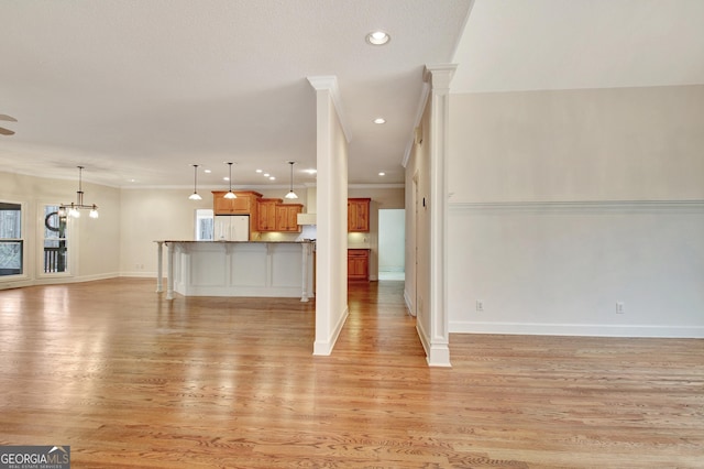 unfurnished living room featuring light wood-type flooring, baseboards, ornamental molding, and a notable chandelier