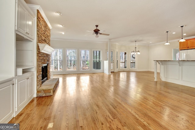 unfurnished living room featuring ceiling fan with notable chandelier, light wood-style floors, a fireplace, and crown molding