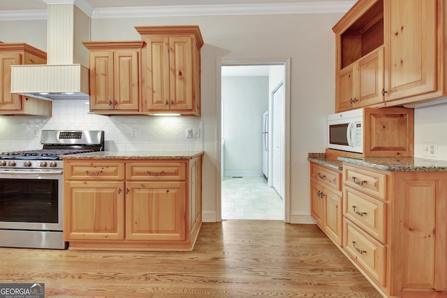 kitchen featuring light wood-style floors, white microwave, light stone countertops, wall chimney range hood, and gas stove