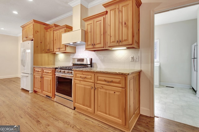 kitchen featuring light stone countertops, backsplash, stainless steel range with gas stovetop, and freestanding refrigerator