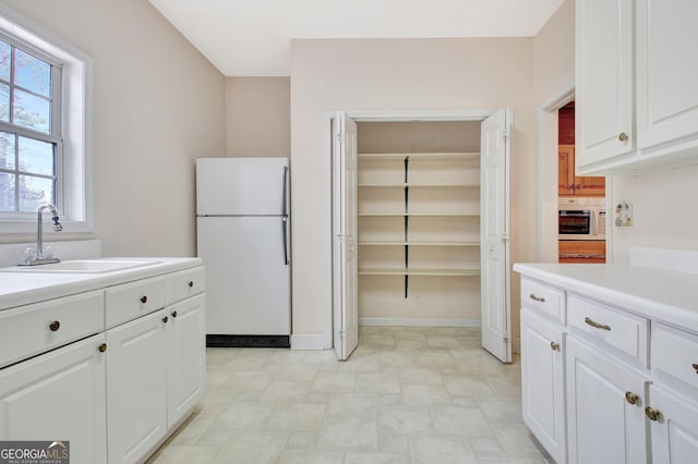 kitchen featuring light countertops, white appliances, a sink, and white cabinetry