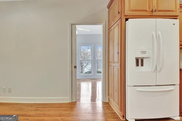 kitchen with light wood-type flooring, white refrigerator with ice dispenser, baseboards, and light brown cabinetry