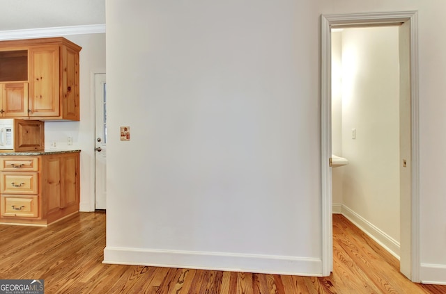 hallway featuring light wood-style floors, ornamental molding, and baseboards