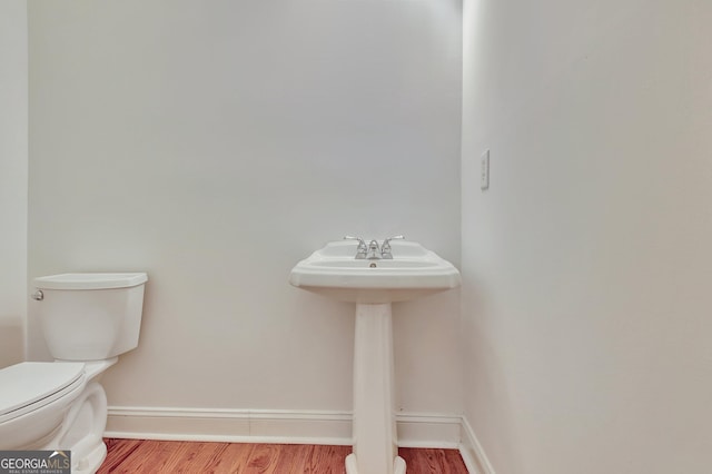 half bathroom featuring wood finished floors, toilet, and baseboards