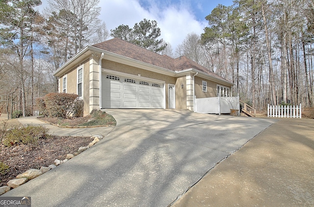 view of side of home with driveway, roof with shingles, an attached garage, fence, and stucco siding