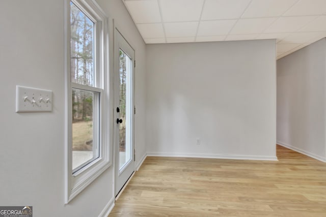 interior space with light wood-style floors, a paneled ceiling, and baseboards