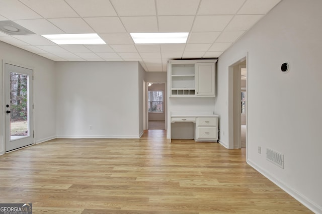 unfurnished living room with built in desk, a paneled ceiling, light wood-type flooring, and visible vents