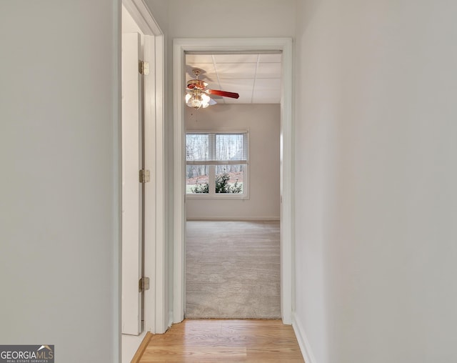 corridor with light carpet, light wood-type flooring, and baseboards