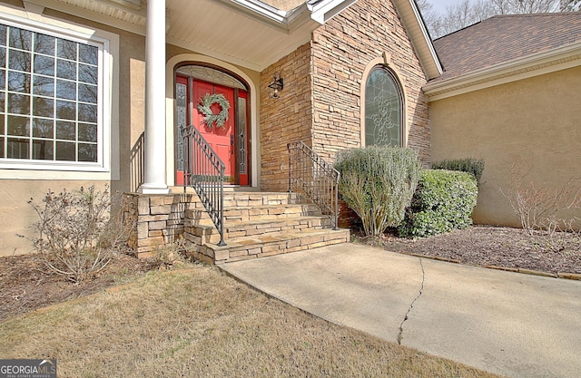 doorway to property featuring brick siding, roof with shingles, and stucco siding