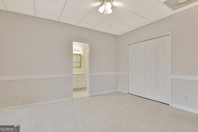 unfurnished bedroom featuring baseboards, a drop ceiling, light colored carpet, ensuite bath, and a closet