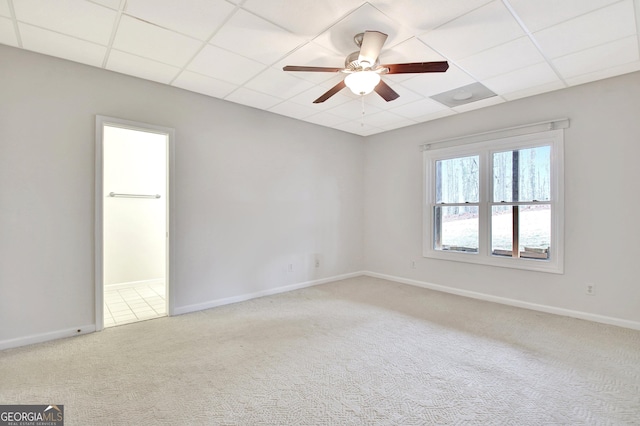 empty room with a paneled ceiling, ceiling fan, baseboards, and light colored carpet