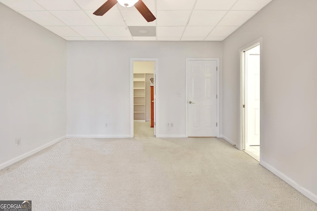 empty room with baseboards, a ceiling fan, a paneled ceiling, and light colored carpet