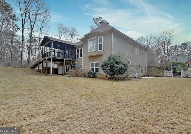 rear view of property featuring a sunroom, stairs, a chimney, and a yard