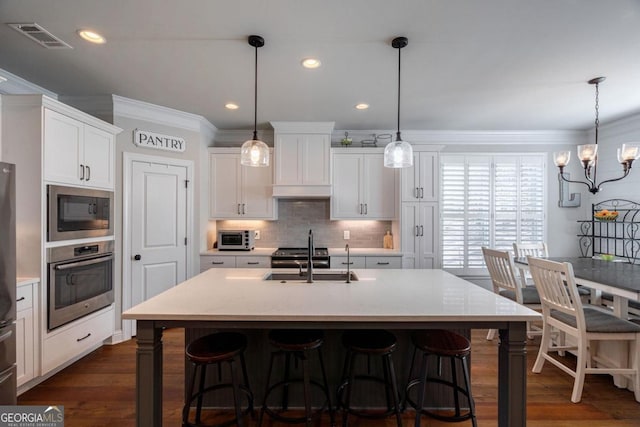 kitchen featuring stainless steel appliances, a sink, visible vents, white cabinets, and hanging light fixtures