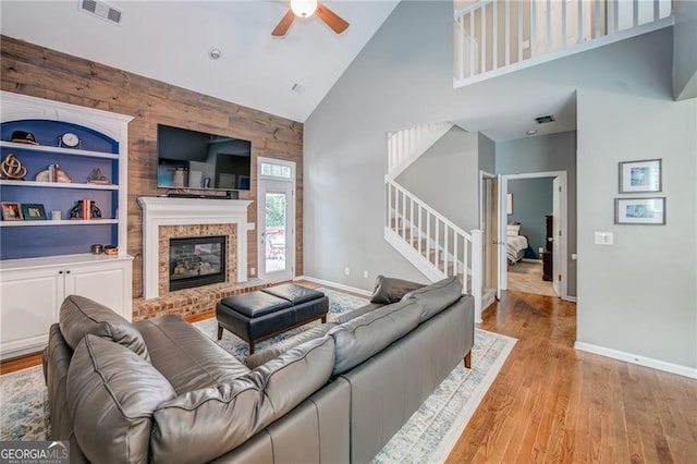 living room with a fireplace, visible vents, built in features, light wood-style floors, and stairway