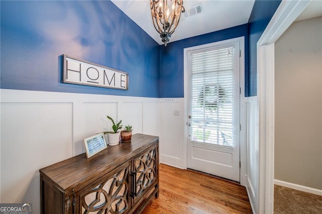 doorway featuring a notable chandelier, visible vents, a decorative wall, wainscoting, and wood finished floors