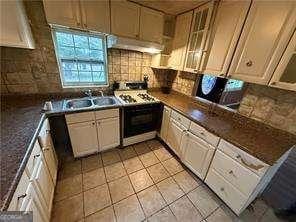 kitchen featuring gas range gas stove, dark countertops, decorative backsplash, a sink, and under cabinet range hood