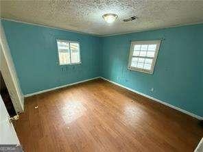 spare room with a wealth of natural light, a textured ceiling, baseboards, and wood finished floors