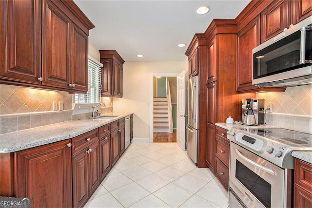 kitchen featuring light stone counters, light tile patterned floors, stainless steel appliances, decorative backsplash, and a sink