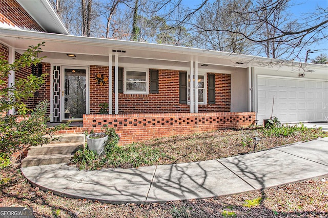 view of exterior entry featuring an attached garage, a porch, and brick siding