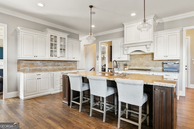 kitchen featuring dark wood-type flooring, an island with sink, gas stovetop, and white cabinetry