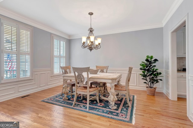 dining area with a wainscoted wall, a notable chandelier, visible vents, light wood-style flooring, and ornamental molding