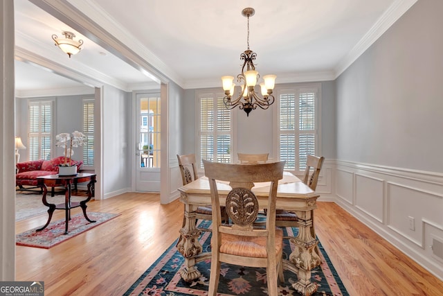 dining room featuring crown molding, light wood-type flooring, a decorative wall, and an inviting chandelier