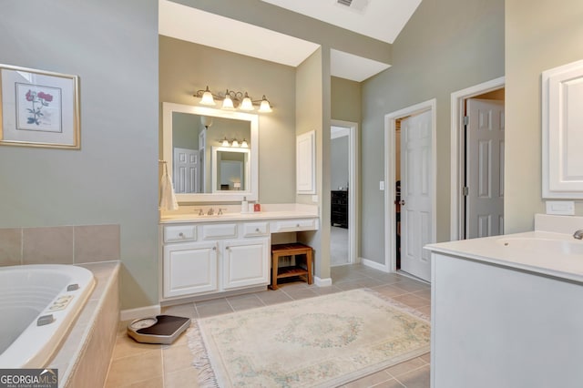 bathroom featuring a relaxing tiled tub, a sink, two vanities, baseboards, and tile patterned floors