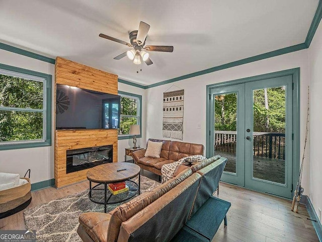 living area featuring ceiling fan, french doors, ornamental molding, light wood finished floors, and a glass covered fireplace