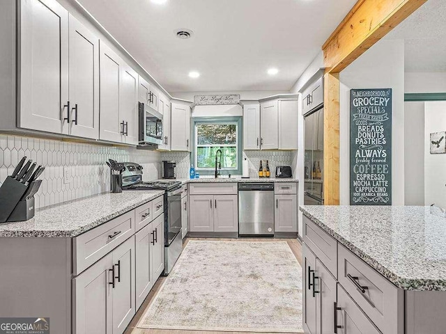 kitchen with visible vents, light stone countertops, gray cabinets, stainless steel appliances, and a sink