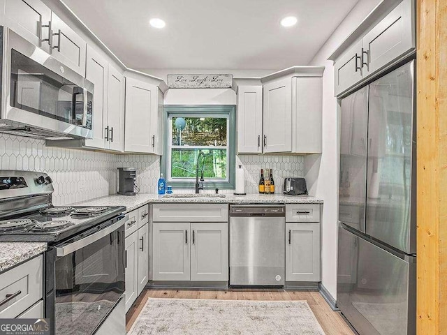 kitchen with appliances with stainless steel finishes, a sink, light wood-style flooring, and light stone countertops