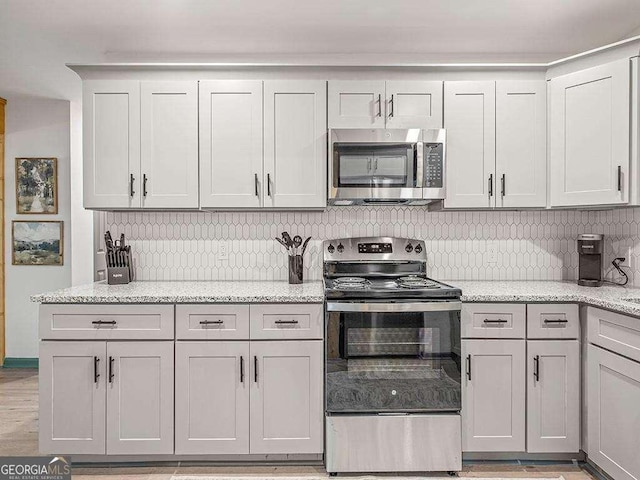 kitchen with tasteful backsplash, light wood-style flooring, appliances with stainless steel finishes, white cabinets, and light stone countertops