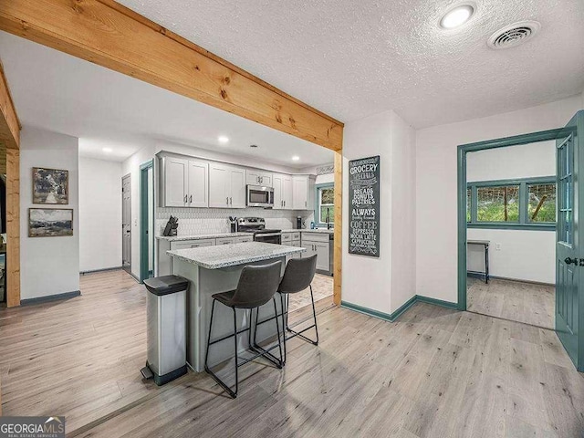 kitchen with a center island, a breakfast bar area, stainless steel appliances, visible vents, and light wood-style floors