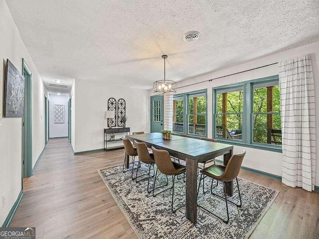 dining room featuring a chandelier, a textured ceiling, light wood-type flooring, and visible vents